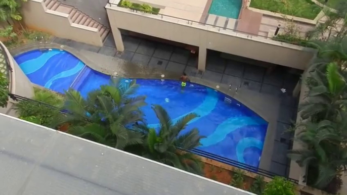 Un garçon saute dans une piscine depuis le toit d'un immeuble