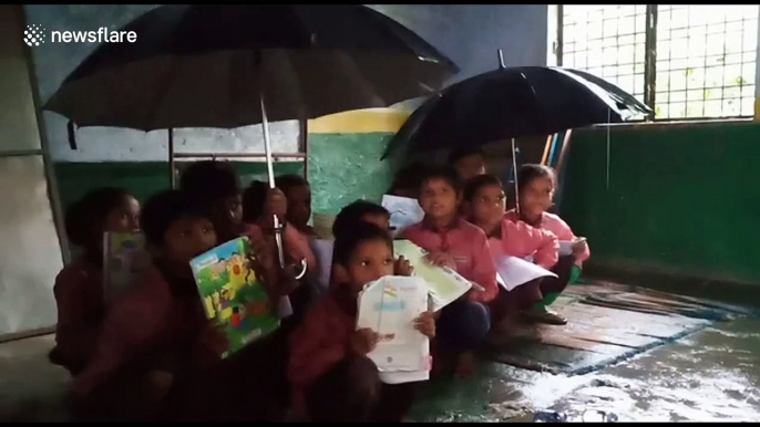 Students in India study with umbrellas in hand as rain leaks through school roof