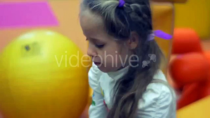 Petite Fille Blonde est Assise sur une Boule de Jouets sur Fond Jouer à des Jeux pour les Enfants