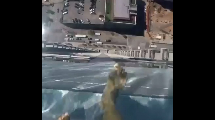 Un homme marche dans une piscine sur le toit d'un immeuble qui a un fond en verre.