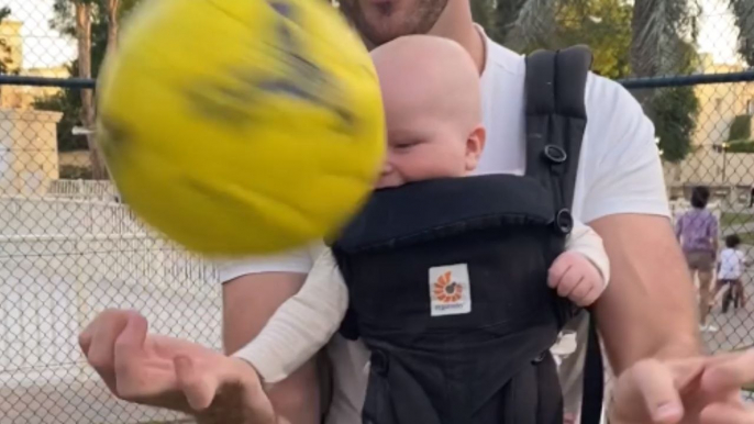 Baby boy giggles with delight as talented dad humors him by spinning ball on finger
