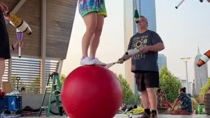 Circus Performer Balances on Ball With Hoop While Men Juggle Pins